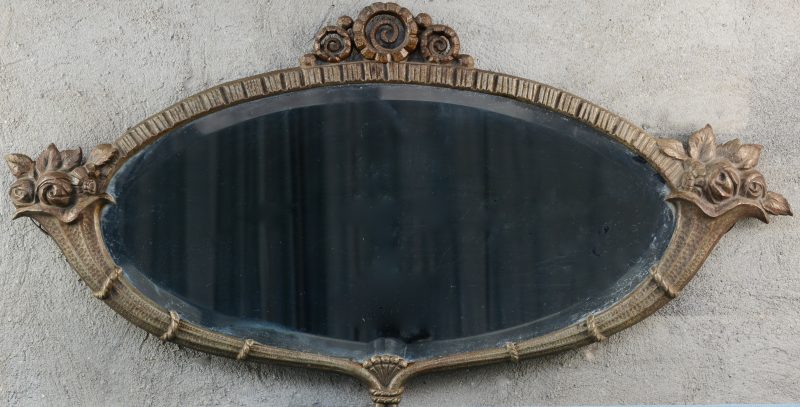 Een ovalen spiegel in ijzeren kader, versierd met bleoemen.