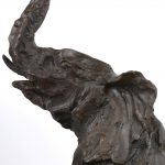 Een bronzen beeld van een zittende olifant op een arduinen sokkel.
