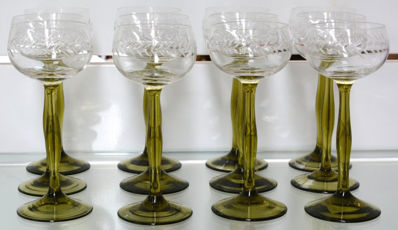 Een reeks van twaalf glazen van geslepen kleurloos kristal op een olijfgroene voet.
