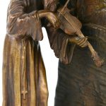 Een bronzen schemerlampje in de vorm van een violist bij een kapel bij een boom met een engeltje.