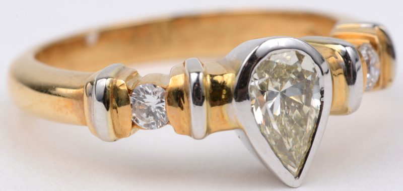 Een 18 wit en geel gouden ring bezet met een centrale peervormige diamant van ± 0,60 ct. en twee briljanten van telkens ± 0,10 ct.