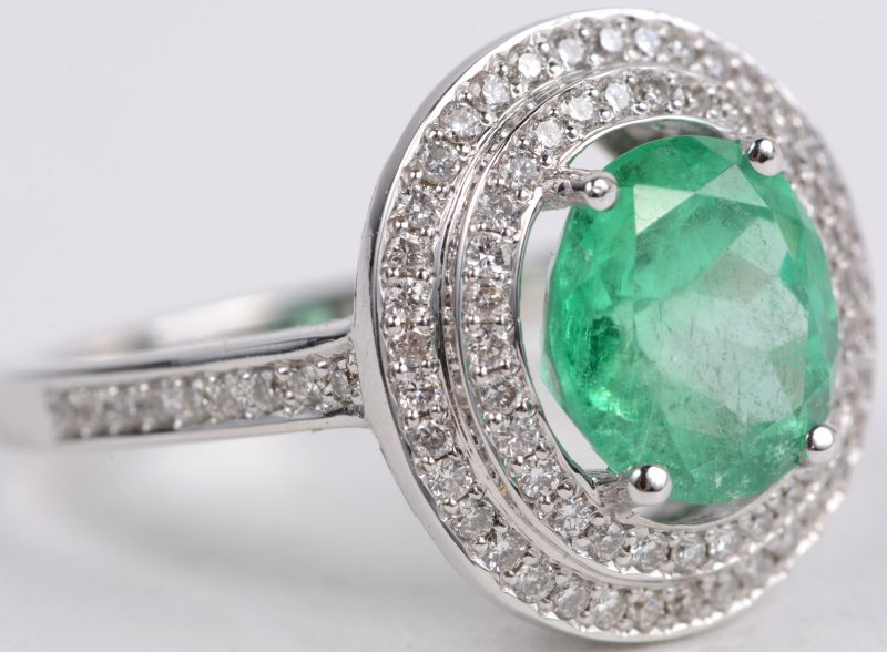 Een 18 karaats wit gouden ring bezet met een centrale smaragd van ± 2,20 ct. en met diamanten met een gezamenlijk gewicht van ± 0,55 ct.