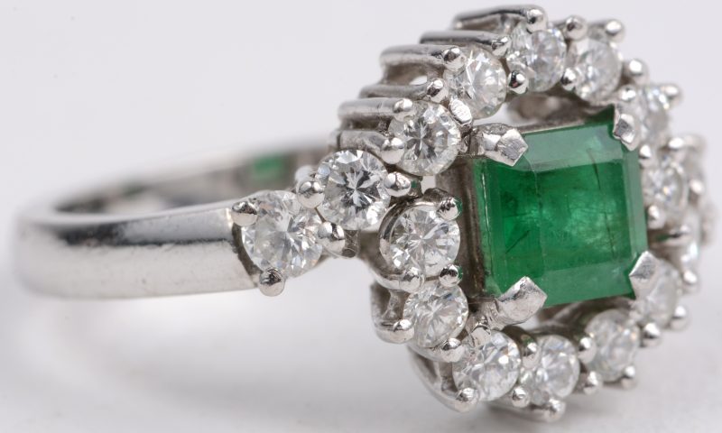 Een platina ring bezet met briljanten met een gezamenlijk gewicht van ± 0,80 ct. en een centrale smaragd van ± 0,50 ct.