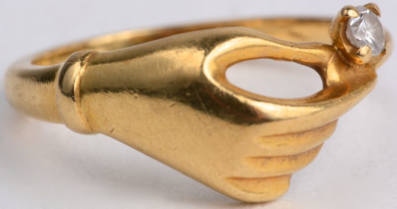 Een 18 karaats geel gouden ring in de vorm van een hand bezet met één briljant van ± 0,05 ct.