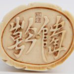 Een beeldje van een godheid met een mand en bloemen. Onderaan gemerkt en met symbool. Chinees werk, eerste helft XXste eeuw. Op een houten sokkeltje.