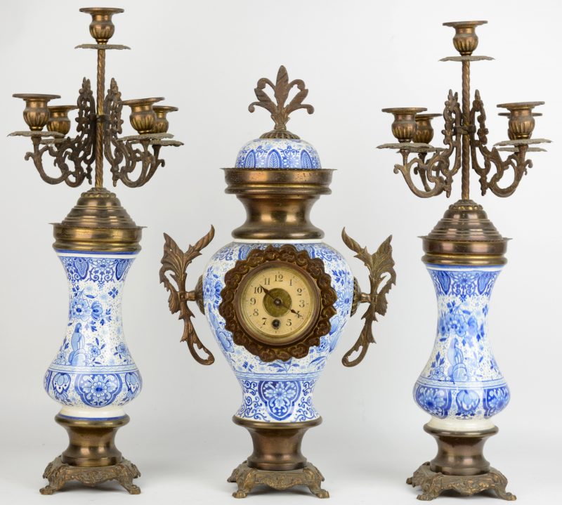 Een driedelig klokstel van koper en blauw en wit aardewerk, bestaande uit een pendule en twee kandelaars.