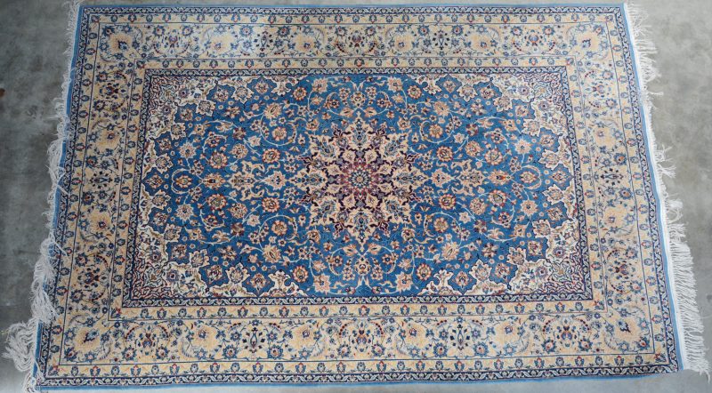 Perzisch tapijt van wol met een centraal medaillon en in lichtblauwe, beige en bruine tonen. Handgeknoopt.