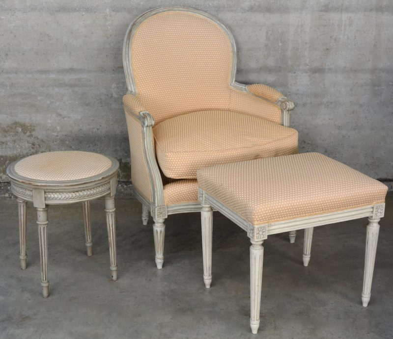 Een fauteuil van gesculpteerd en witgepatineerd hout in Lodewijk XVI-stijl met een bijpassend rond en rechthoekig voetbankje.