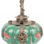 Een pompoenvormig theepotje van Chinees porselein met een decor van bloemen op groene fond en met koperen monturen.
