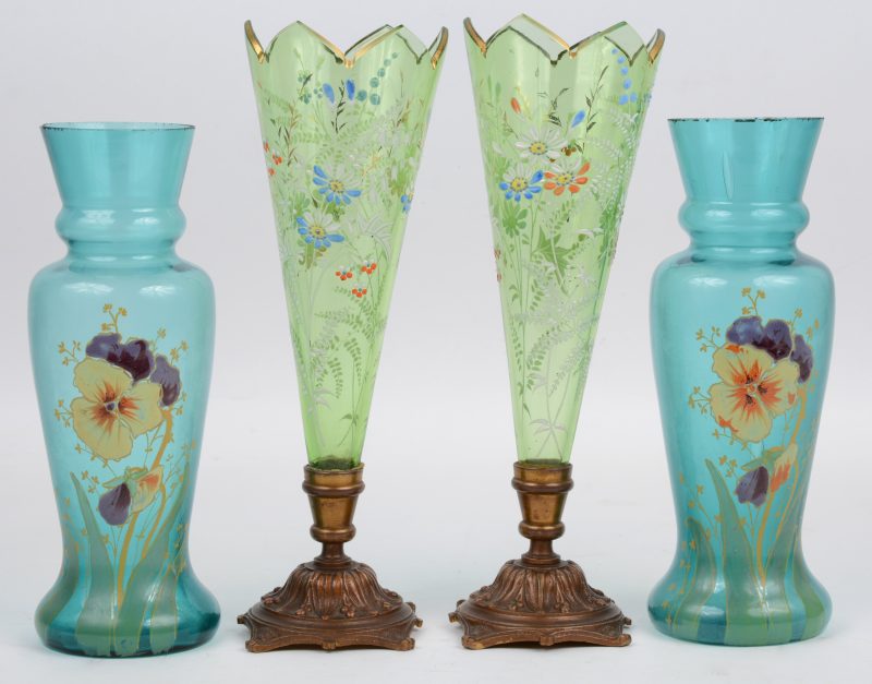 Een lot XIXe eeuws glas met handbeschilderde bloemendecors, bestaande uit twee fluitvaasjes op koperen voet en twee balustervaasjes.