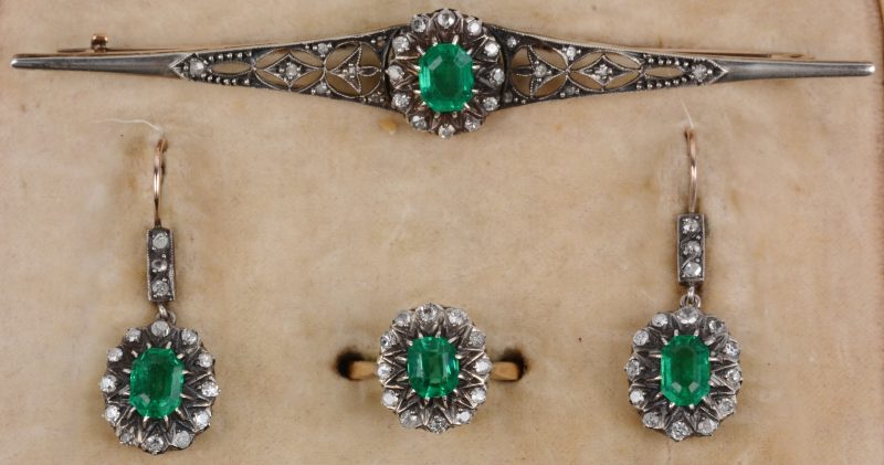 Een 18 karaats wit en geel gouden ring met bijpassende oorbellen en een broche bezet met diamanten met een gezamenlijk gewicht van ± 1 ct. en smaragden met een gezamenlijk gewicht van ± 4 ct.