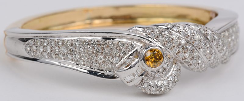 Een 18 karaats wit en geel gouden slavenarmband bezet met briljanten en baguettes met een gezamenlijk gewicht van ± 6 ct. en een centrale fancy diamond van ± 0,50 ct.