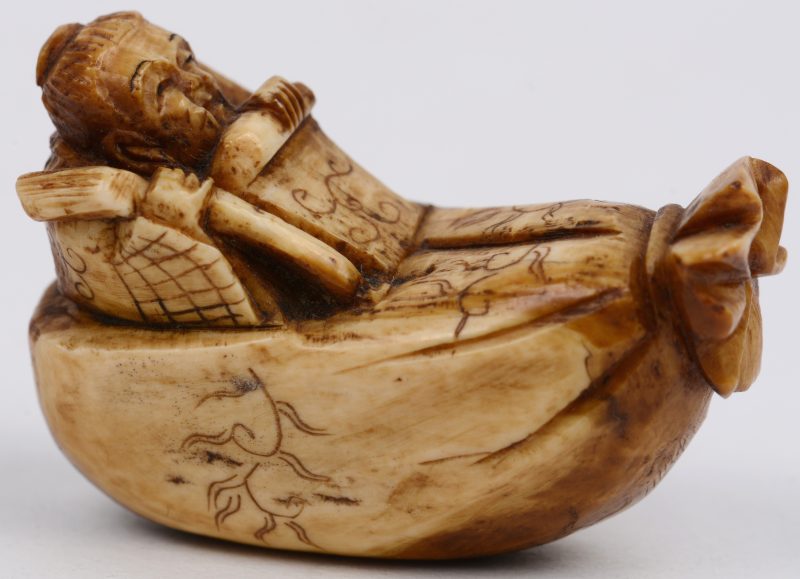 Een antieke netsuke van gesculpteerd ivoor in de vorm van een liggende wijze.