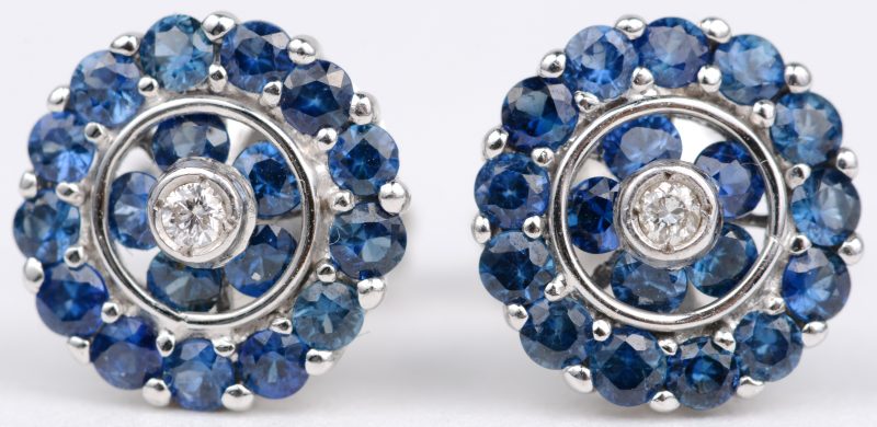 Een paar 14 karaats wit gouden oorbellen bezet met twee kleine diamantjes  en met saffieren met een gezamenlijk gewicht van ± 1,60 ct.