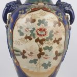 Een vaas van Japans aardewerk met een decor van een krijger en een geisha en van bloemen in cartouches.