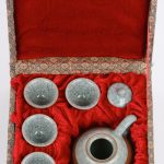 Een miniatuur theepotje met vier borreltjes van grijs crackleware. In etui.