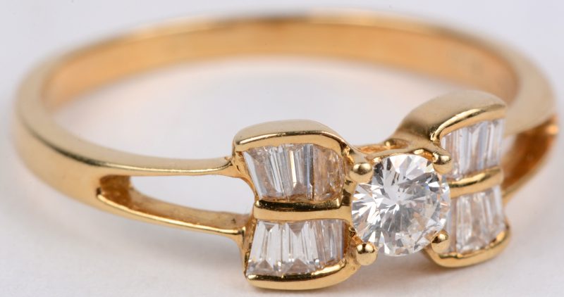 Een 18 karaats geel gouden ring bezet met een centrale diamant van ± 0,20 ct. en diamant baguettes met een gezamenlijk gewicht van ± 0,50 ct.