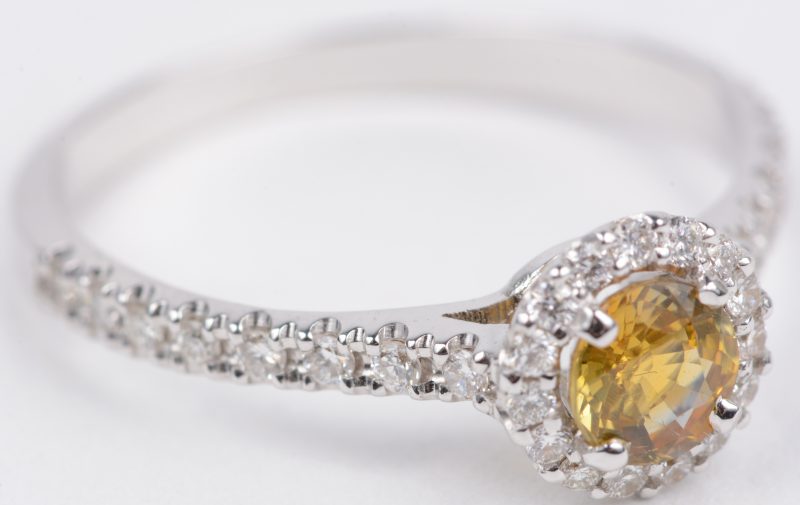 Een 18 karaats wit gouden ring bezet diamanten met een gezamenlijk gewicht van ± 0,25 ct. en een gele saffier ± 0,54 ct.