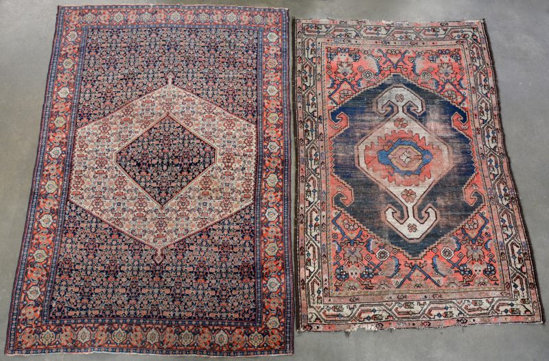 Twee verschillende handgeknoopte Oosters karpetten, waarbij één met slijtage en de andere met een kleine scheur aan het uiteinde.