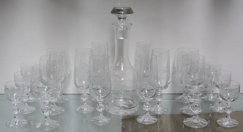 Een glazenservies van kleurloos kristal met een gegraveerd decor, bestaande uit een karaf, zes borrelglaasjes, zes wijnglazen en zes champagnefluiten.