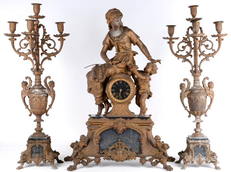 Een bronzen pendule, getooid met een zittende vrouw, met twee kandelaars met telkens vier lichtpunten, versierd met hermenfiguren.
