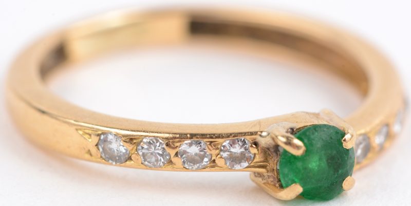 Een 18 karaats geel gouden ring bezet met kleine briljanten en één smaragd met een klein letsel.