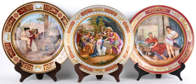 Drie schotels van polychroom porselein, met de hand beschilderd. Achteraan gemerkt en twee ervan met een opschrift: “Römischen Vasenverkaufer” en “Pyrrhäus beschutz Adromache”. Wenen, XIXde eeuw.