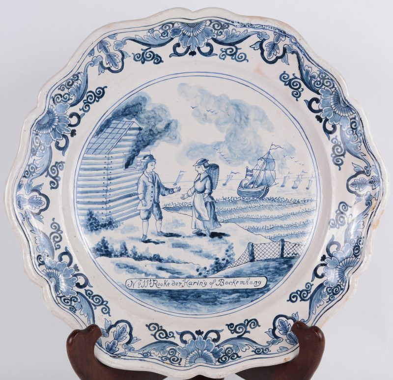 Een Delfts blauwe schotel met een vissersscène en het opschrift “N° 11. Rooke der Haring of Bockemhang”. Achteraan gemerkt Lambertus Cleffius, De Metaale Pot. XIXe eeuw. Kleine restauratie.