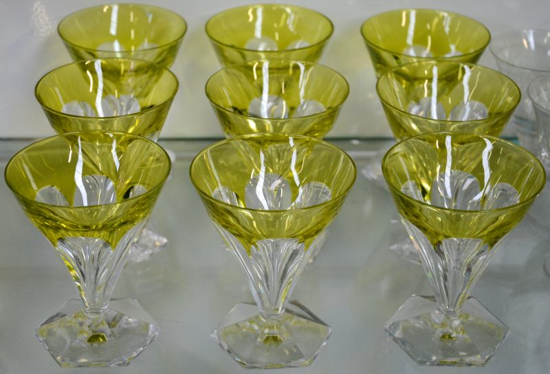 Een reeks van negen glaasjes van geslepen kristal, de kelk groen gekleurd in de massa en op zeshoekige voet. Eén met letsels.