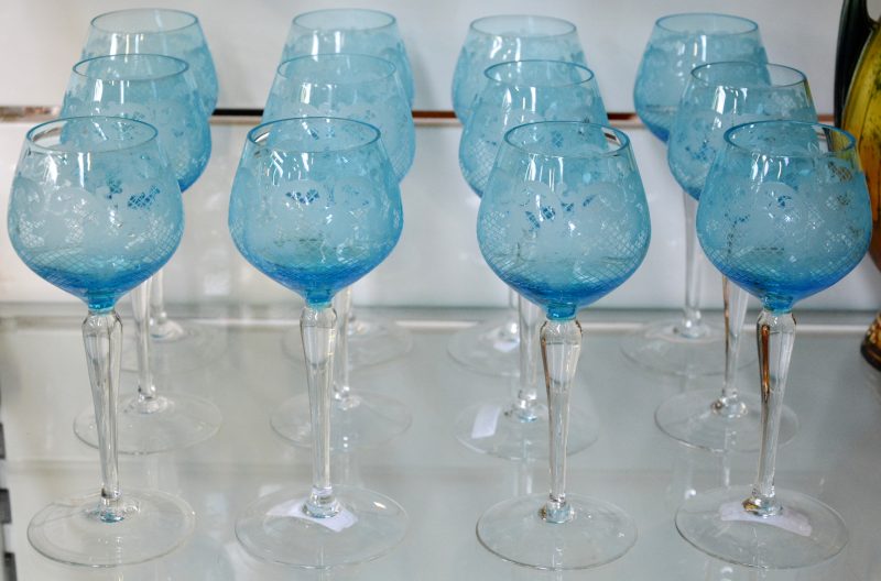 Een reeks van twaalf glazen van kleurloos en blauw kristal met een geslepen decor.