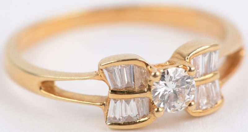 Een 18 karaats geel gouden ring bezet met een centrale briljant van ± 0,20 ct. en diamant baguetten met een gezamenlijk gewicht van ± 0,60 ct.