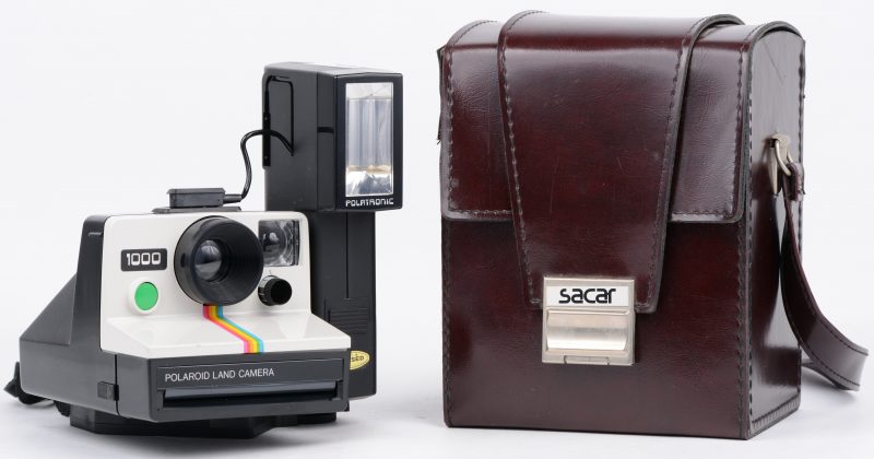 Een Polaroid 1000 land camera voor SX-70 film. Met flash en statiefbevestigingsstuk en in lederen draagtas.