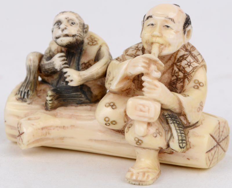 Een netsuké van gebeeldhouwd ivoor. meet voorstelling van een pijproker en een aap op een boomstronk. Japans werk, begin XXste eeuw. Onderaan gemerkt.
