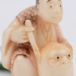 Een netsuké van gebeeldhouwd ivoor met voorstelling van een zittende man en vergezeld van een kleine inro met ojime, met een gegraveerd decor. Japans werk, begin XXste eeuw. Onderaan gemerkt.