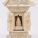 Een miniatuurpagode van been en ivoor met een reliëfdecor van planten, personages en vogels. Achter twee deurtjes een zittende Boeddha. Eén dakspant manco. China, eerste deel XXste eeuw.