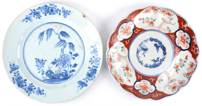 Twee borden van Aziatisch porselein, waarbij één Imari en het andere Chinees met een blauw en wit decor van planten.