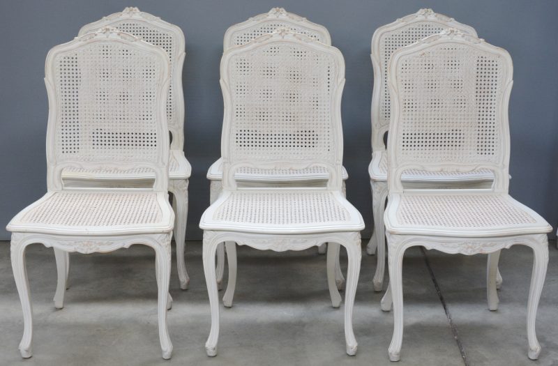 Een serie van zes licht grijze gecanneerde stoelen.