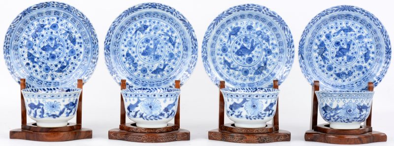 Vier theekopjes en schoteltjes van blauw en wit Chinees porselein versierd met vissen. Een schilfer aan een kop en één aan een schoteltje. Met houten staandertjes.