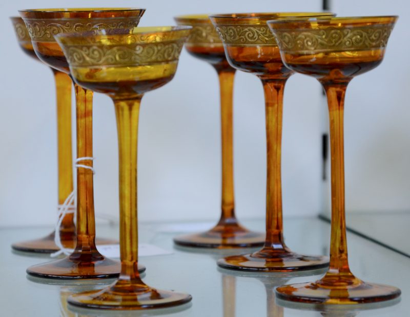 Een serie van zes amberkleurige glazen borreltjes op voet. Versierd met een vergulde fries. Begin XXe eeuw.