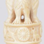 Een klein schemerlampje van gesculpteerd ivoor met een decor van dieren in de jungle. Met boven aan het Indische staatssymbool. Indisch werk. Op houten sokkel. Omstreeks 1930.