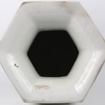 Een zeshoekige vaas van monochroom wit porselein naar het blanc de Chine met een decor van planten en voorwerpen in reliëf.