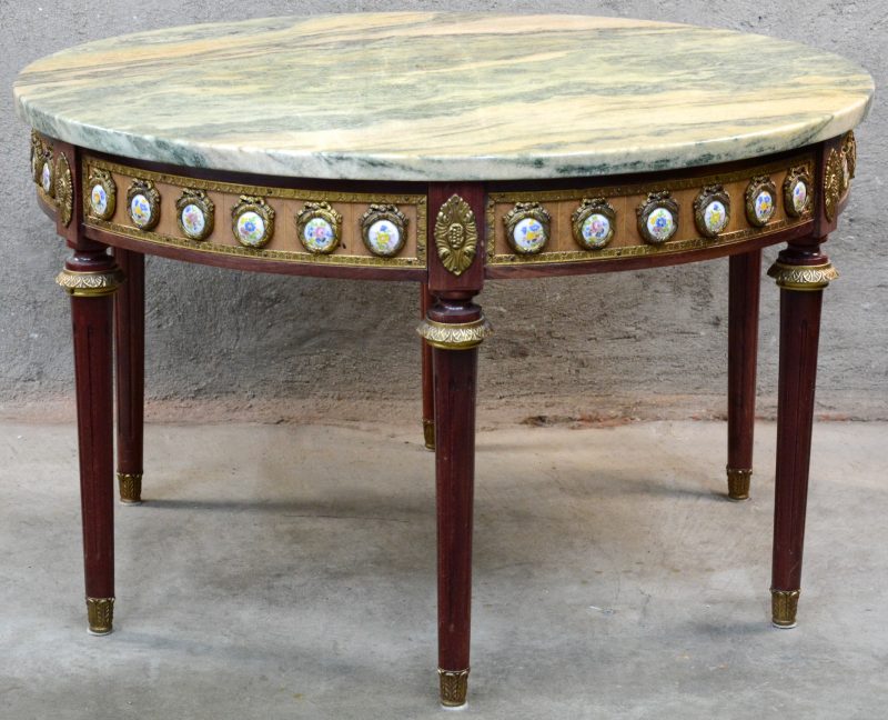 Een ronde gefineerde salontafel met marmeren blad, rondom versierd met porseleinen plaquettes.