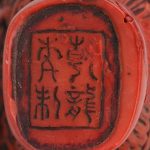 Een snuffbottke van Chinese rode lak met een reliëfdecor van Boeddha’s. Onderaan gemerkt.