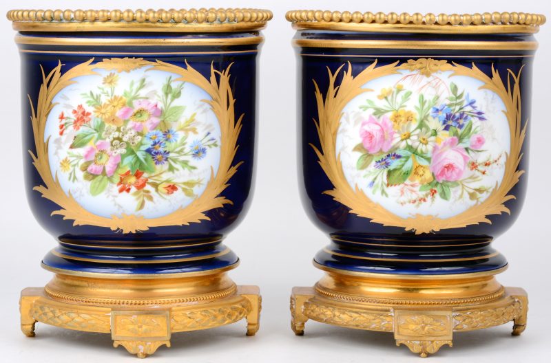 Twee cachepots van Sèvresporselein met een meerkleurig decor van personages en bloemen in vergulde uitsparingen en op kobaltblauwe fond. Met verguld koperen montuur en voet. Onderaan gemerkt. Omstreeks 1900.