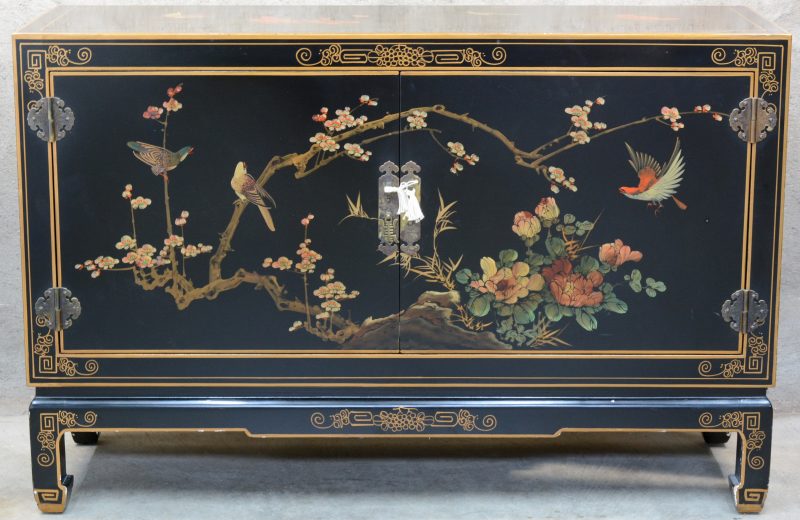Een Chinese tweedeurskastje van zwartgelakt hout, versierd met een decor van bloeiende takken en vogels.