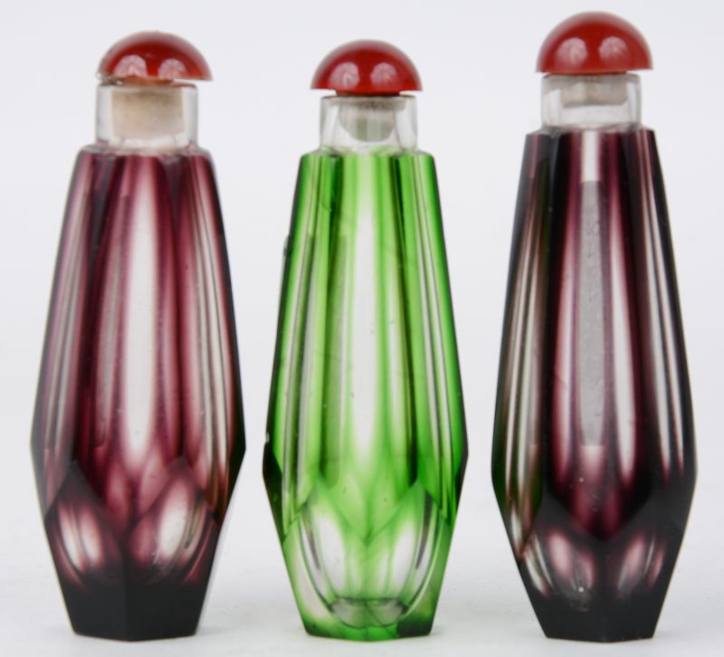 Drie parfumflesjes van handgeskepen kristal, waarbij twee paars en één groen gekleurd in de massa.