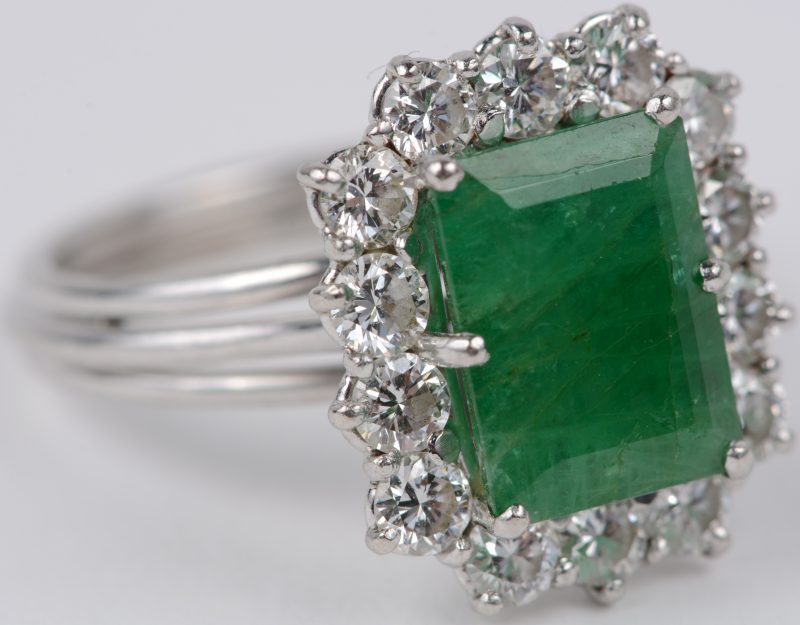 Een 18 karaats wit gouden ring bezet met een centrale smaragd van ± 3 ct. en briljanten met een gezamelijk gewicht van ± 1,40 ct.