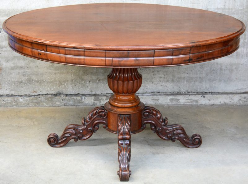 Een verlengbare ronde tafel van mahoniehout met een gebeeldhouwde centrale poot, eindigend in vier voluten.