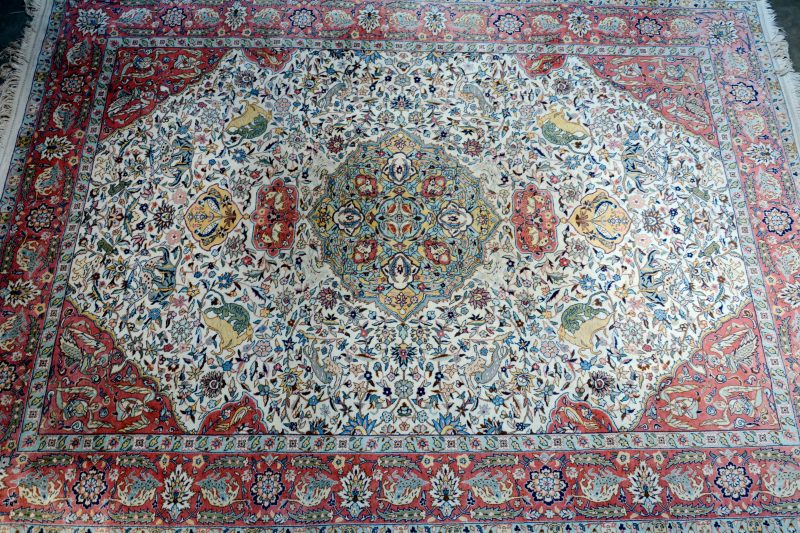 Een handgeknoopt Perzisch wollen tapijt met een decor van dieren en bloemen.