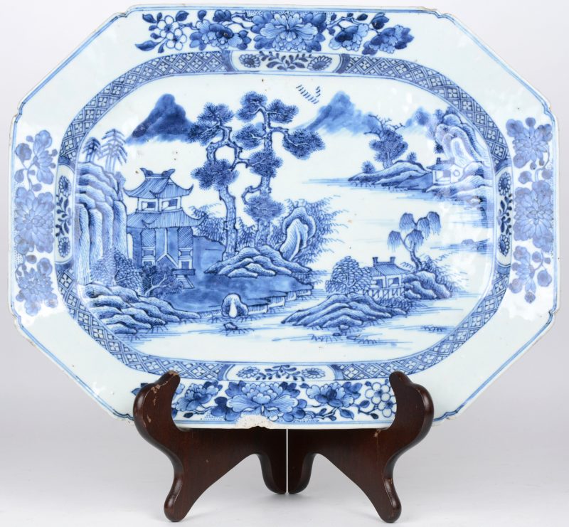 Een achthoekige schotel van Chinees porselein met een blauw op wit landschapsdecor. Schilfer.